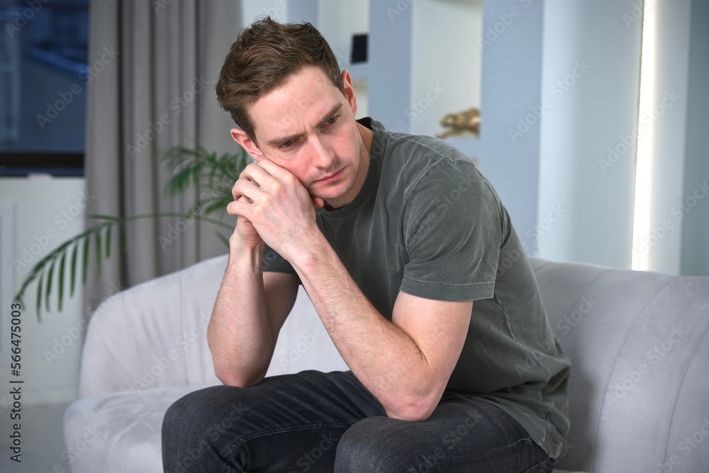 Sad upset depressed unhealthy guy, young tired exhausted frustrated man is suffering at home, sitting on couch or sofa, having headache, migraine. Failure, despair, depression concept Sad upset depressed unhealthy guy, young tired exhausted frustrated man is suffering at home, sitting on couch or sofa, having headache, migraine. Failure, despair, depression concept
