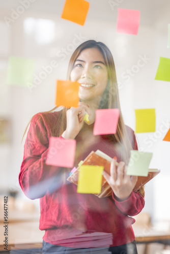 Asian businesswoman creating project plan on office wall with sticky paper notes. stylish confident manager working on business, financial and marketing planning projects. 