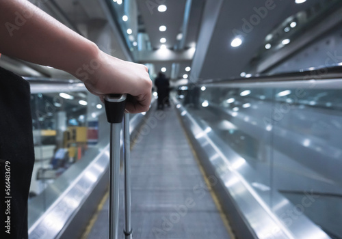 Traveller female holding suitcase on escalator at airport or transit flight with luggage on holiday traveling in elevator arriving at international airport.