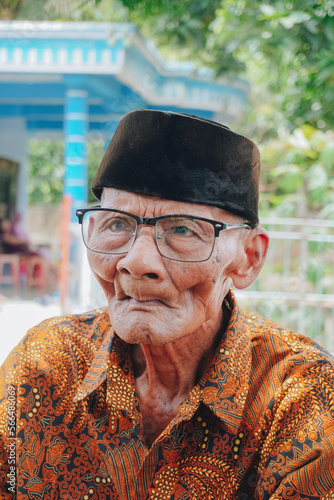 A portrait of an old Asian man wearing batik shirt and glasses photo