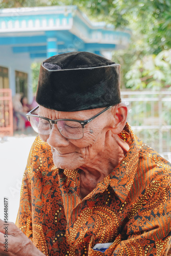 A portrait of an old Asian man wearing batik shirt and glasses photo