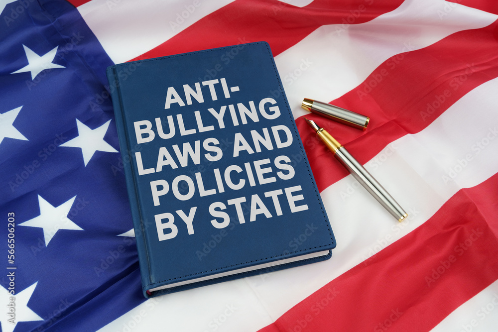 On the US flag lies a pen and a book with the inscription - ANTI-BULLYING LAWS AND POLICIES BY STATE