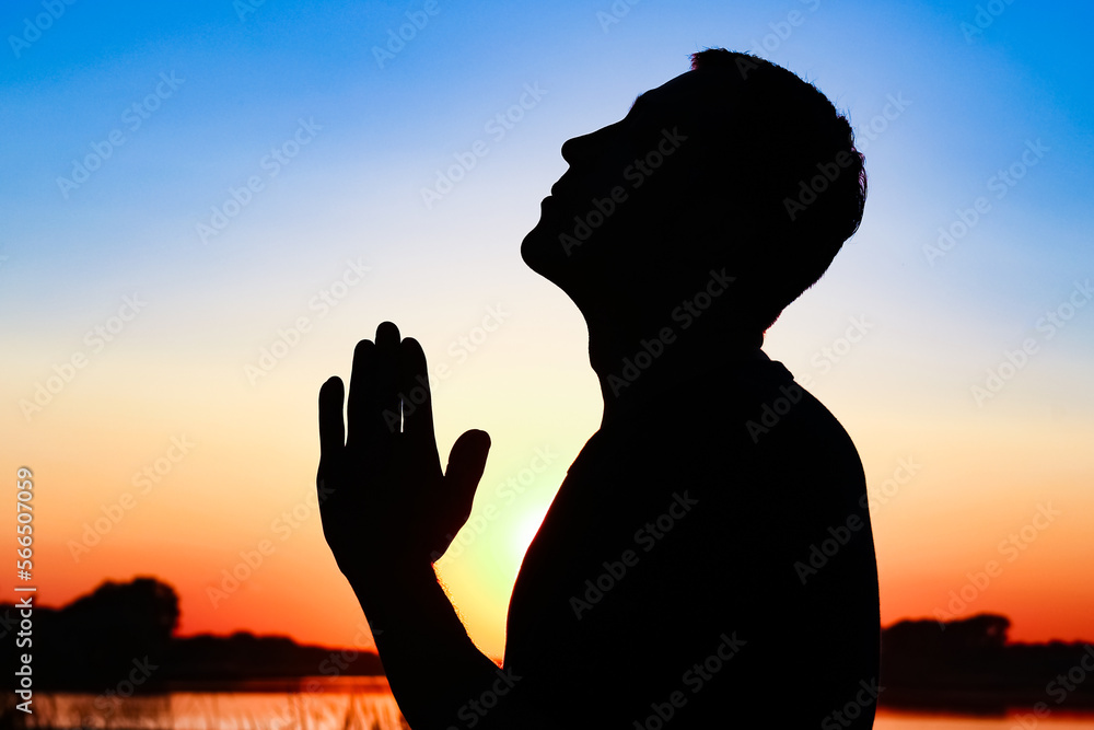 Silhouette of man praying at sunset background