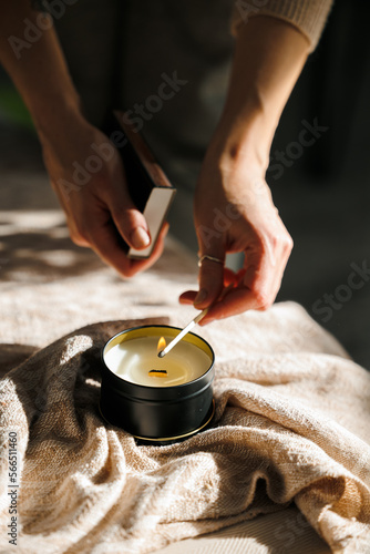 Soy scented candles in metal jars, boxes. The candle is lit by a girl. A long match burns.  Modern handmade coconut wax candles without paraffin. 
