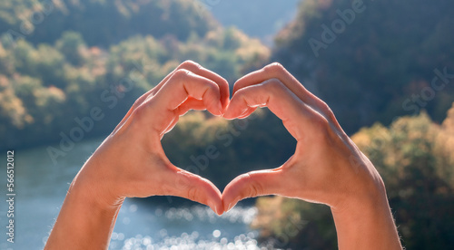 Love nature  travel  Earth day concept. Shape of heart  made by women hands on backgroubd of beautiful natural landscape - water surface of mountain lake and forested green mountains. Panoramic banner