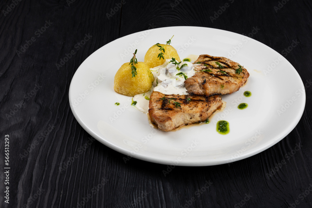 Grilled pork meat with mushroom sauce and potato on white plate on wooden black background Grilled pork meat with mushroom sauce and potato on white plate on wooden black background
