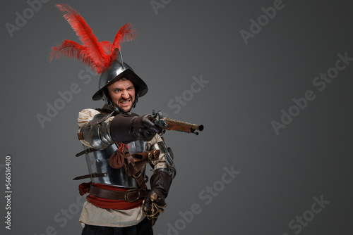 Portrait of antique furious musketeer dressed in steel plate armor holding pistol.