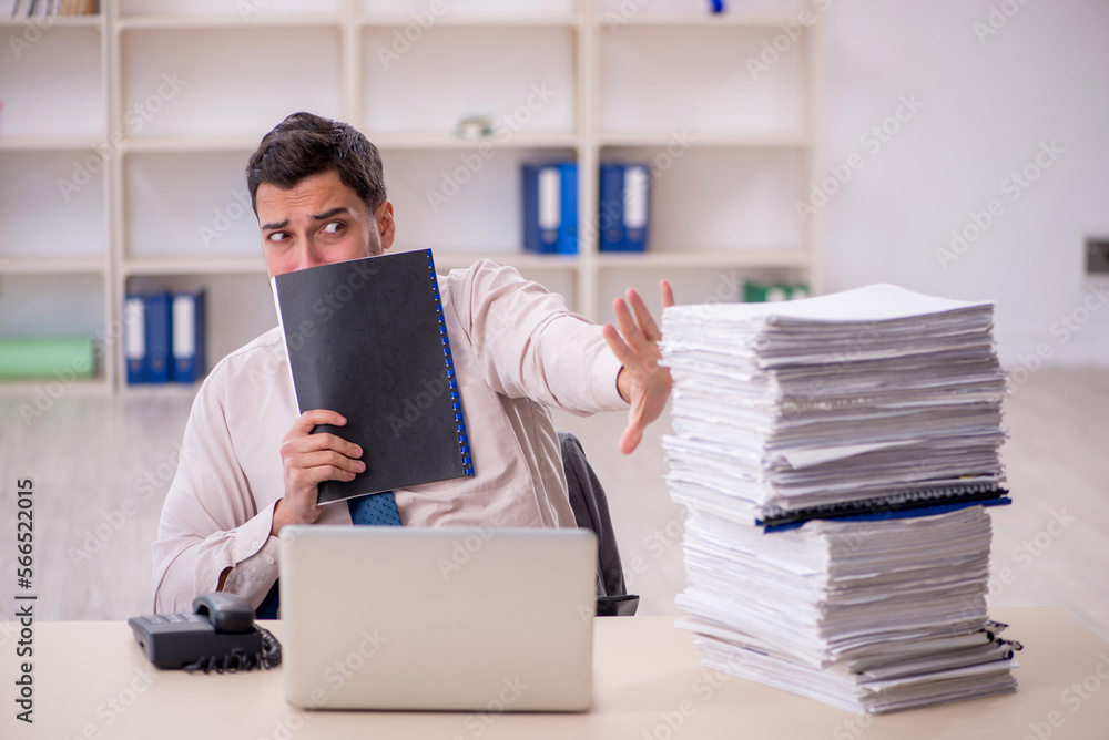 Young male employee unhappy with excessive work in the office Young male employee unhappy with excessive work in the office
