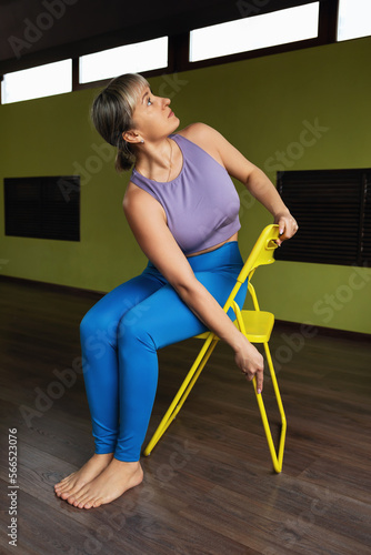 A woman leading a healthy lifestyle and practicing yoga therapy, performs a turn on a chair, trains in a modern studio