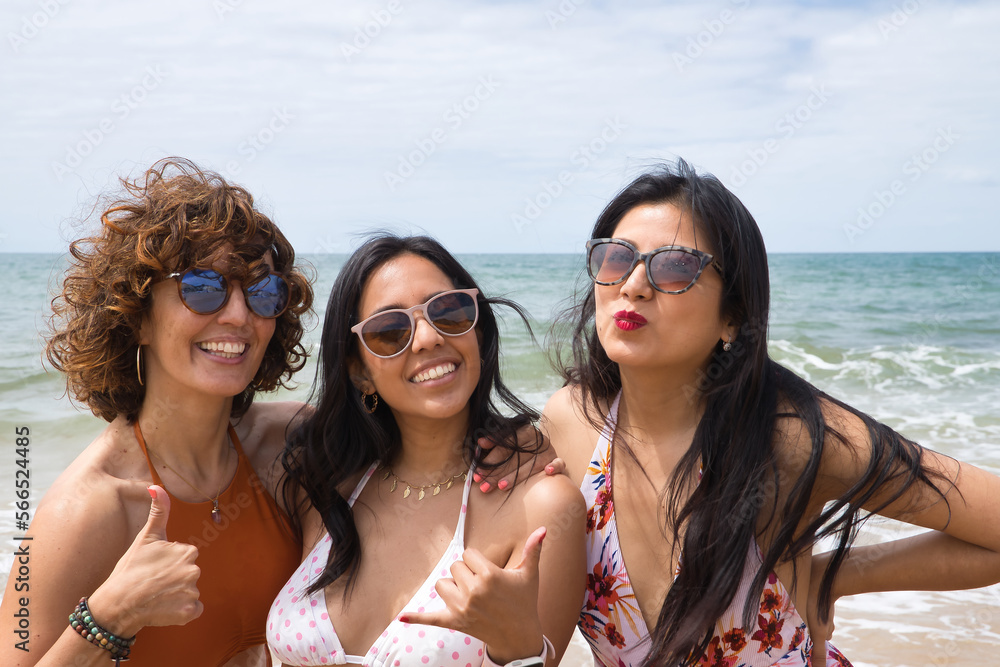 Attractive mature woman next to two young, pretty, brunette South American women in bikinis and sunglasses taking funny pictures of each other. Concept vacation, friends, multiethnic, summer.