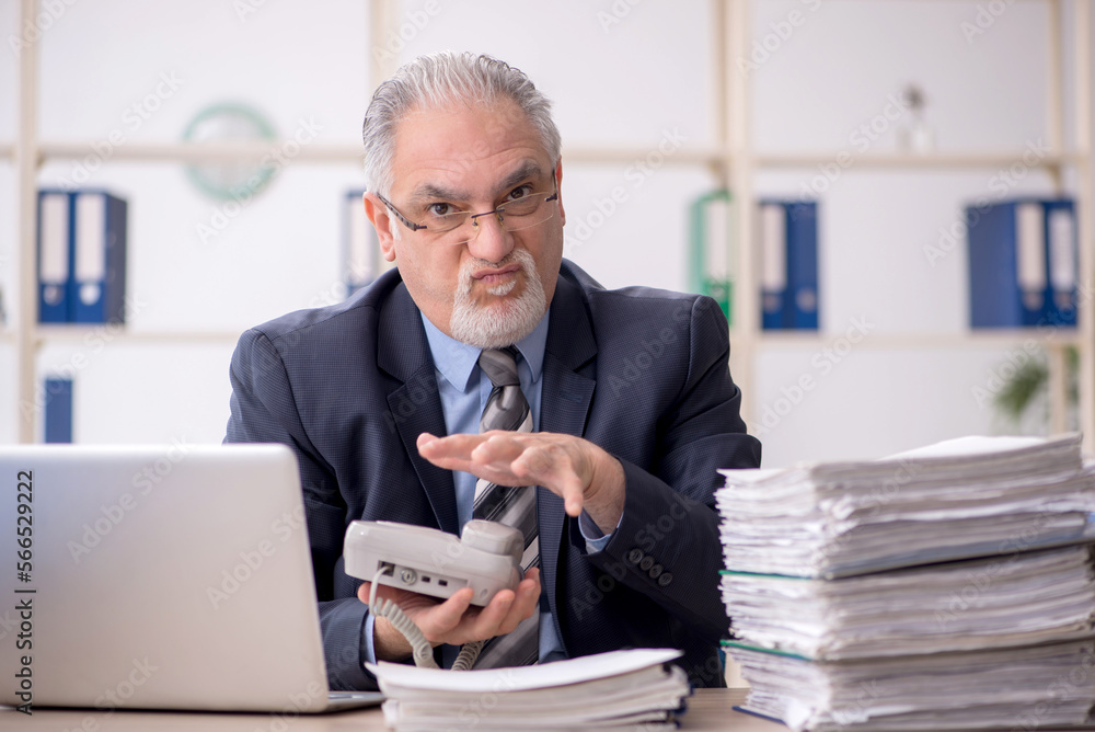 Old male employee speaking by phone in the office