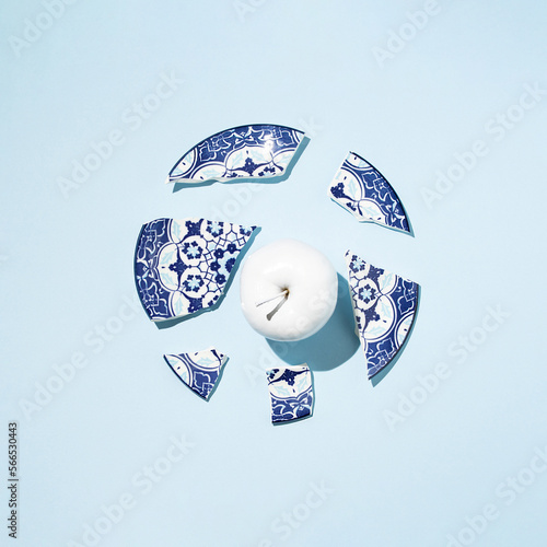 Photography Fresh apple colored in white paint and broken china porcelain plate on blue background