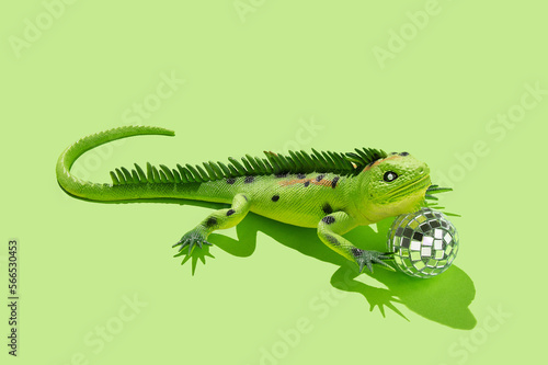 Iguana lizard toy with disco ball on green background. Minimal concept. Copy space.