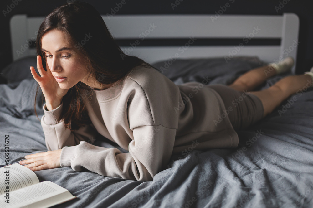 Young brunette woman reading a book in her bed in the morning. Shot of a young woman reading a book while relaxing at home. Weekend. Young brunette woman reading a book in her bed in the morning. Shot of a young woman reading a book while relaxing at home. Weekend.