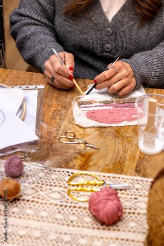 Embroidery punch needle workshop. Middle-aged woman with red painted nails applies glue on embroidered fabric.