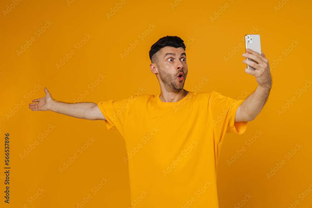 Surprised man taking selfie with outstretched hand isolated over yellow wall Surprised man taking selfie with outstretched hand isolated over yellow wall