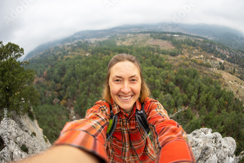 female tourist taking a selfie portrait on top of a mountain - Happy smiling woman using her smartphone - Hiking and rock climbing. © zhukovvvlad