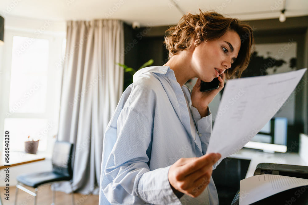 Young businesswoman talking on mobile phone while standing in office Young businesswoman talking on mobile phone while standing in office