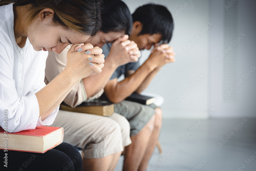 A group of Asian Christians sits inside a Catholic Church praying for God's blessing, the pale sun shining in the place of worship with copy space. A group of Asian Christians sits inside a Catholic Church praying for God's blessing, the pale sun shining in the place of worship with copy space.