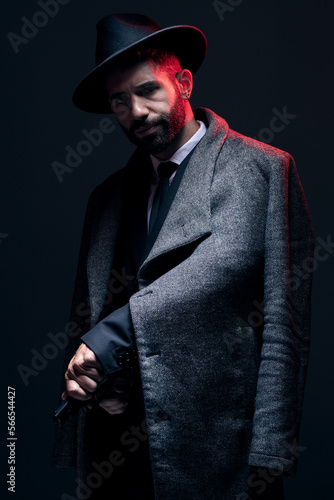 Gangster, portrait and holding gun on studio background in dark secret spy, isolated mafia leadership or crime lord security. Model, man and hitman suit weapon in formal or fashion clothes aesthetic