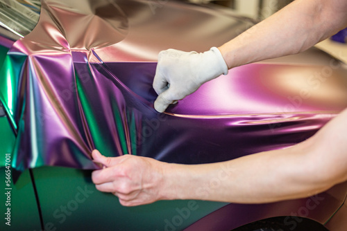 A specialist in wrapping a car with chameleon-colored vinyl film in the process of work. Car wrapping specialists cover the car with vinyl sheet or film. Selective focus.