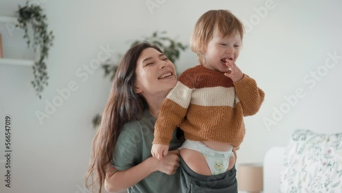 Young loving mother dresses beautiful infant boy kid, caring parent putting on sweater, do morning routine on baby toddler bright bedroom. Care, fashion comfort clothes, parenthood, cherish, babyhood