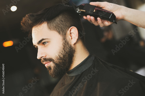 Professional hairdresser working with bearded client in barbershop