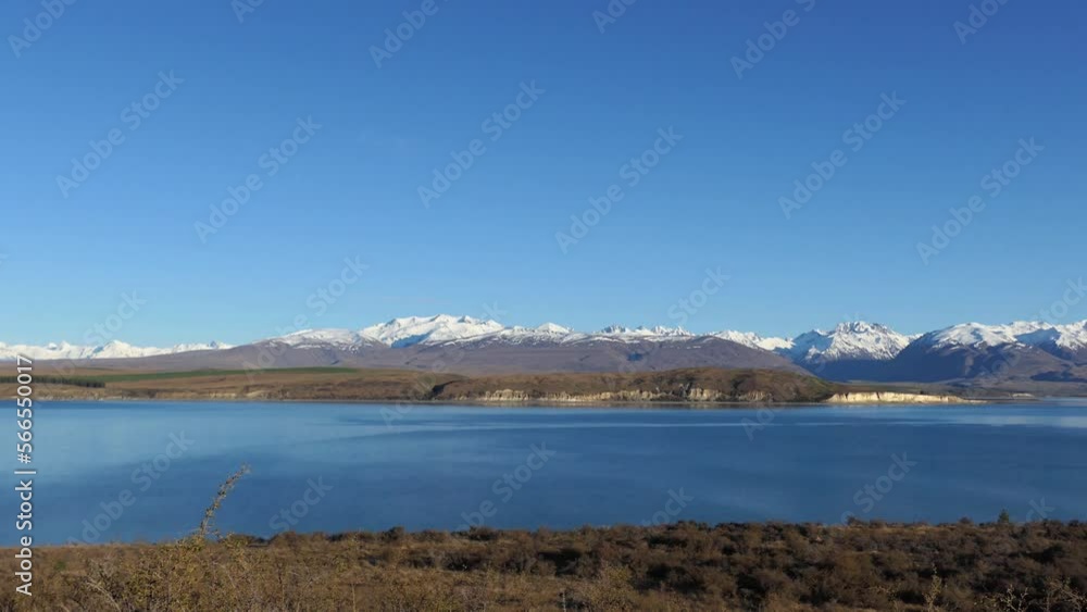 Golden-hour, mid-winter pan across beautiful inky blue alpine lake with majestic mountains in distance (Lake Tekapo and Southern Alps, New Zealand) Golden-hour, mid-winter pan across beautiful inky blue alpine lake with majestic mountains in distance (Lake Tekapo and Southern Alps, New Zealand)