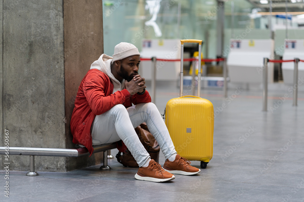 Sad African American man upset at airport his flight is delayed. Depressed traveler male waiting for a plane sitting in empty terminal with baggage. Exhausted guy on a long night connection at airport Sad African American man upset at airport his flight is delayed. Depressed traveler male waiting for a plane sitting in empty terminal with baggage. Exhausted guy on a long night connection at airport
