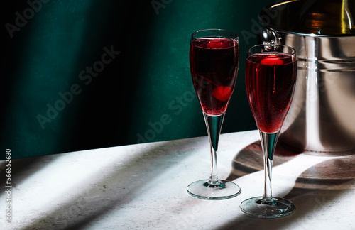Kir Royale alcoholic cocktail with blackcurrant liqueur, prosecco and cocktail cherry. Dark green background, hard light and shadow pattern photo