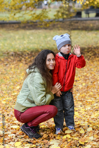 Young mother with her little son in the park against the background of autumn foliage.