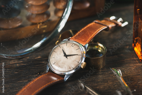 Vintage men's Omega dress watch with white rustic dial and brown leather strap laying on the dark brown rustic wooden table near to the instruments.