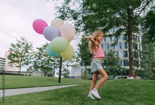 Little blond girl posing with baloons in city and looking at camera. © Halfpoint