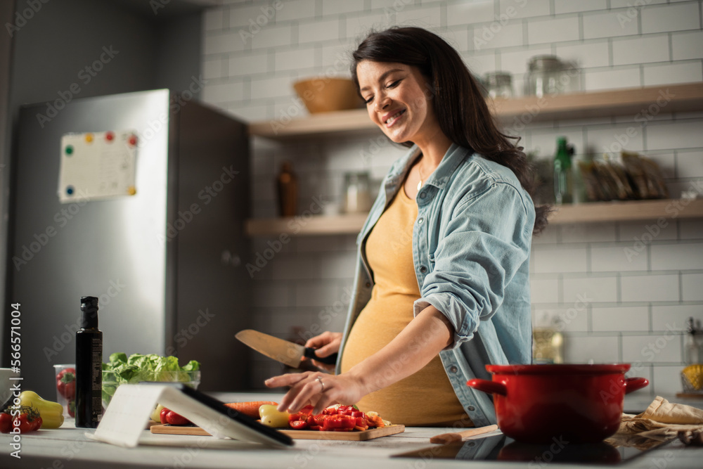 Young woman cutting vegetables in kitchen. Beautiful pregnant woman making salad