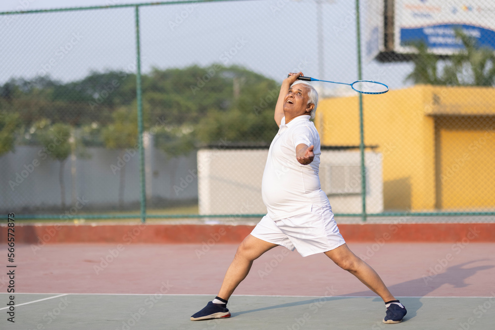Senior man playing badminton outdoor at badminton court. Concept of active lifestyle being on pension