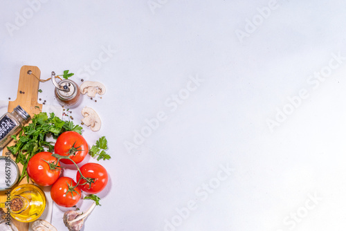 Cooking background with vegetable ingredients. Healthy dinner preparation flat lay, with fresh raw tomatoes, onion, garlic, herbs and greens, olive oil, salt, pepper seasonings, on white background 