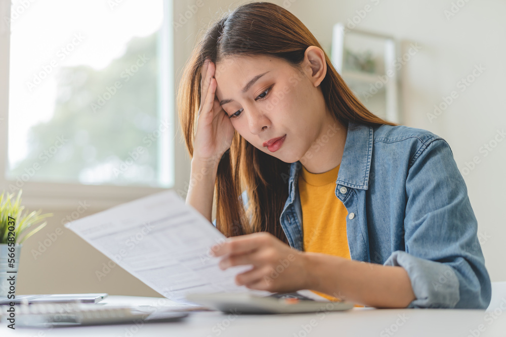 Young Asian woman looking at credit card invoice in her hands and worry about cash on bills payday Young Asian woman looking at credit card invoice in her hands and worry about cash on bills payday