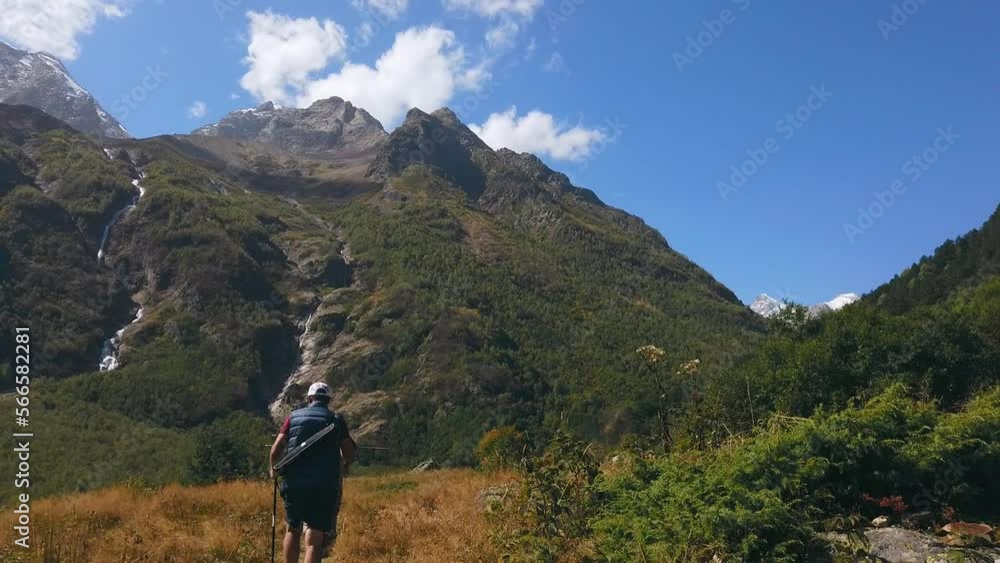 Two tourists travel with a backpack on their shoulders in the mountains. Friends go along the mountain path to the waterfalls Two tourists travel with a backpack on their shoulders in the mountains. Friends go along the mountain path to the waterfalls