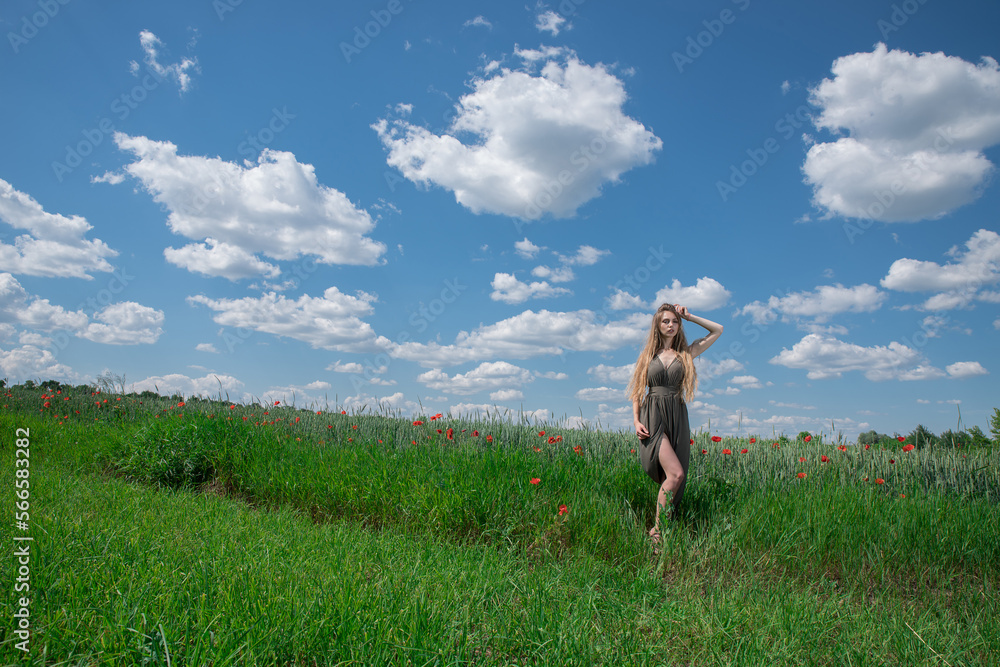 Girl in a wheat field with poppies under a summer cloudy sky.