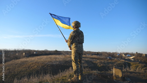 Portrait of soldier in military uniform lifted up flag of Ukraine in hill. Ukrainian army man holding waving flag. Victory against russian aggression. Invasion resistance concept. Slow motion photo