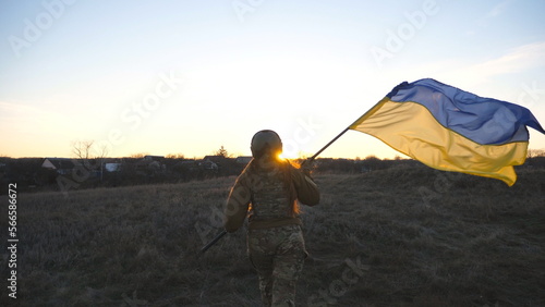 Female ukrainian army soldier runs and waves flag of Ukraine at sunset. Woman in military uniform lifted up flag in honor of the victory against russian aggression. Invasion resistance concept. Slowmo