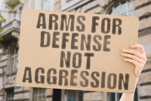 The phrase " Arms for Defense, Not Aggression" is on a banner in men's hands with blurred background. Protect. Shield. Guard. Safe. Armed. Safekeeping. Defend. Military. Protection. Guarded. Safely © AndriiKoval