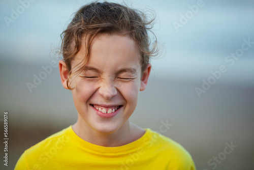 Close-up shot of a boy laughing with eyes closed tight. Happy child with curly hair in yellow t-shirt. Outdoor view against blurry background. Expecting a surprise © danr13