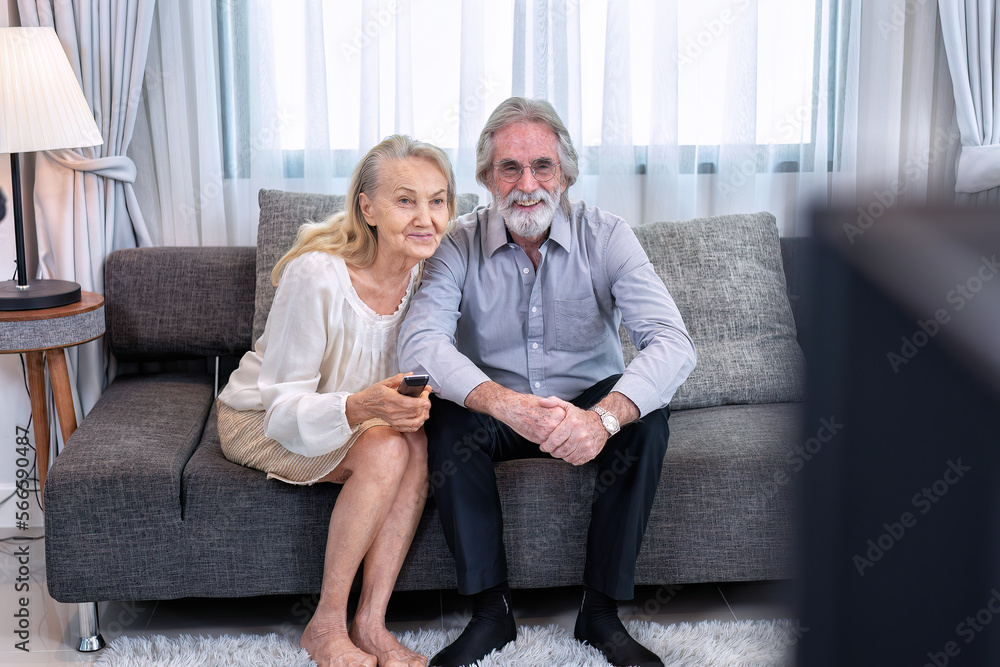 Obraz premium Elderly couple Joyful sitting on sofa use remote control select TV channel being in a great mood