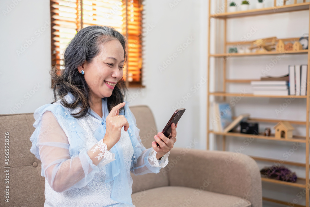 An elderly businesswoman in her hand holding a smartphone looks at the information about the company she is a senior boss inside the house and happily eats snacks and drinks coffee, Concept of WFH. An elderly businesswoman in her hand holding a smartphone looks at the information about the company she is a senior boss inside the house and happily eats snacks and drinks coffee, Concept of WFH.