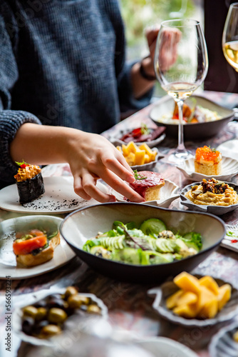 woman hand eating food in restaurant. wine, cheese, meat, vegetables and other appetizers on table