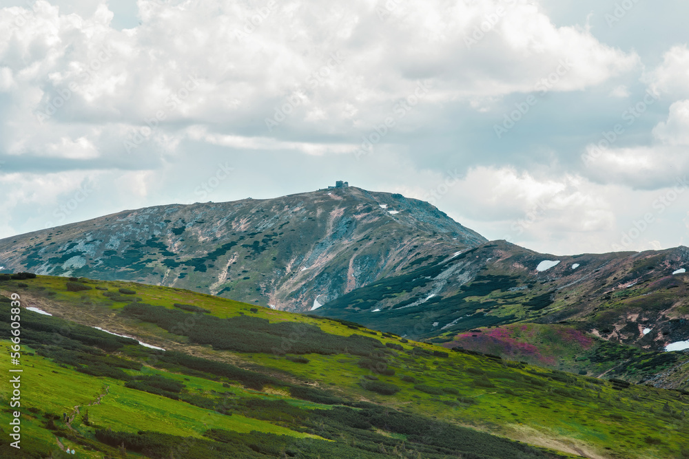 View of Carpathian mountains in summer, meadows, rocks, sky and clouds, flowers and snow, abandoned observatory at the top Pip Ivan, amazing landscape and background, part of hiking and trekking trail