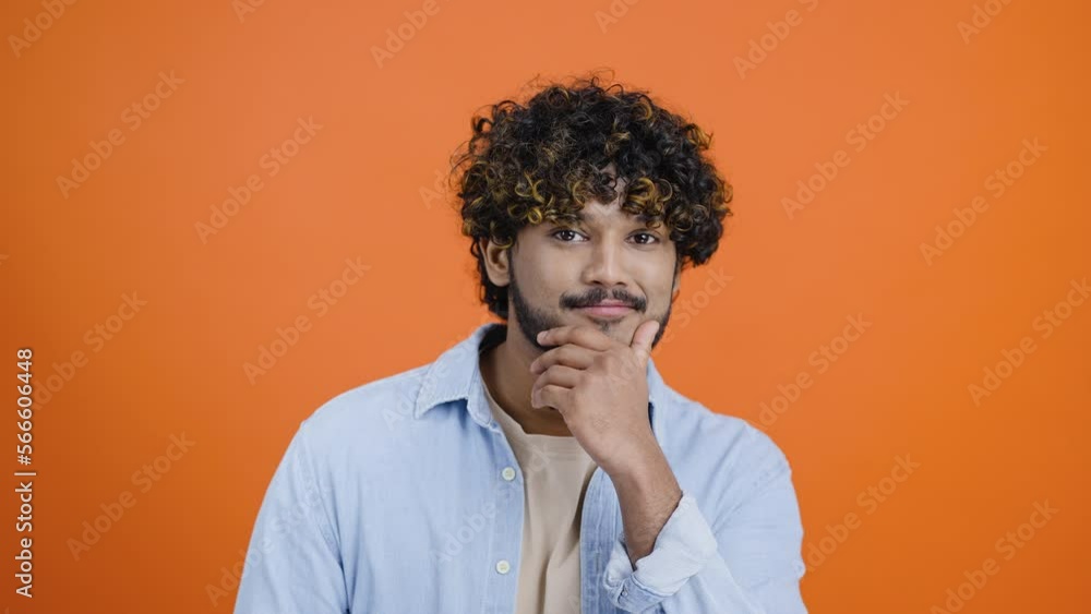 Handsome Indian man winks and rubs beard looking in camera Handsome Indian man winks and rubs beard looking in camera