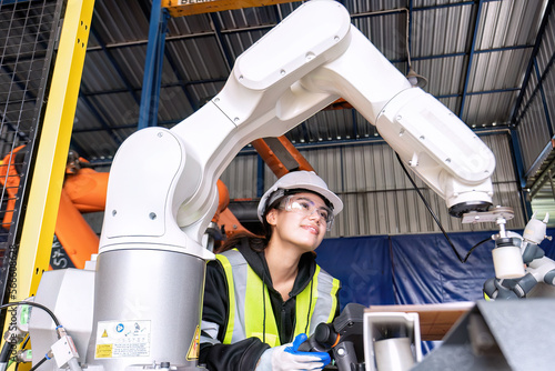 Young female asian service engineer holding robot controller operate robot arm automation factory