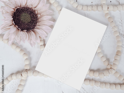White, blank card invitation mock-up with pink sunflowers with natural wooden beads on a white table